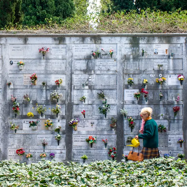  A woman carries a watering can past a wall of funerary niches at the San Michele island cemetery in Venice, Italy.