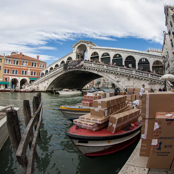 The Rialto Bridge serves as a backdrop for delivery barges on the Grand Canal.