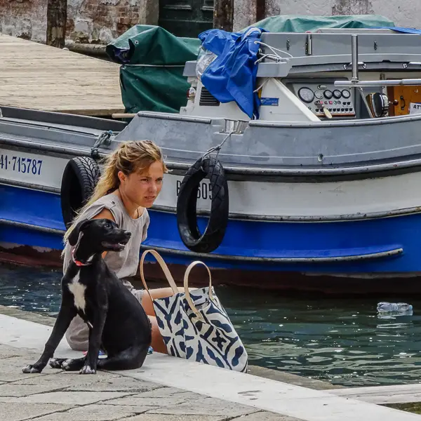  A young woman and her dog relax on a fondamenta with a barge behind them.